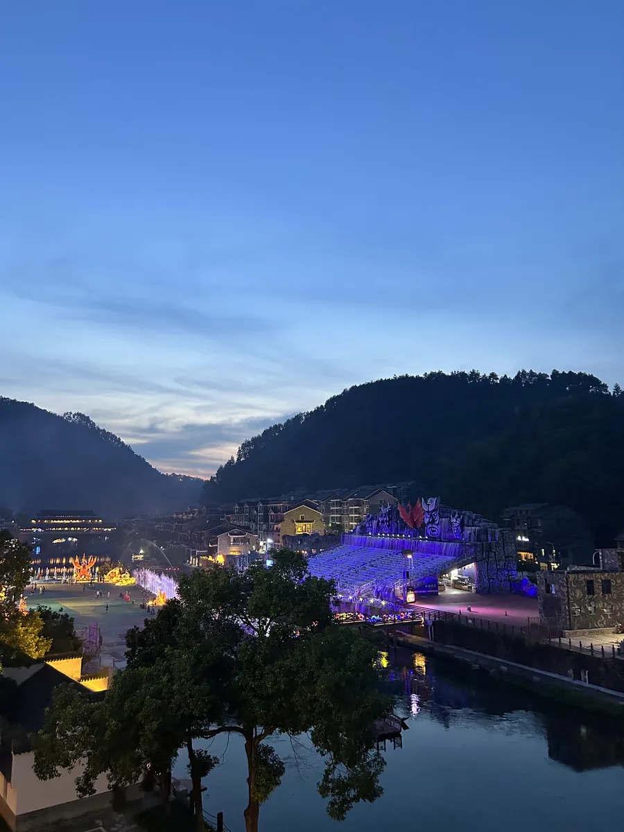 The Tuo River and Fenghuang's hills at blue hour, the town lights just beginning to glow against a deep-blue dusk sky.