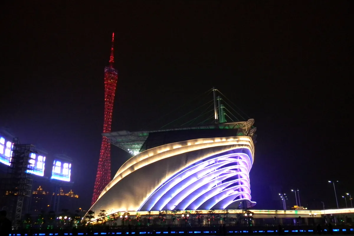 The Canton Tower's red-lit spire beside the illuminated, wave-shaped Guangzhou Opera House at night.