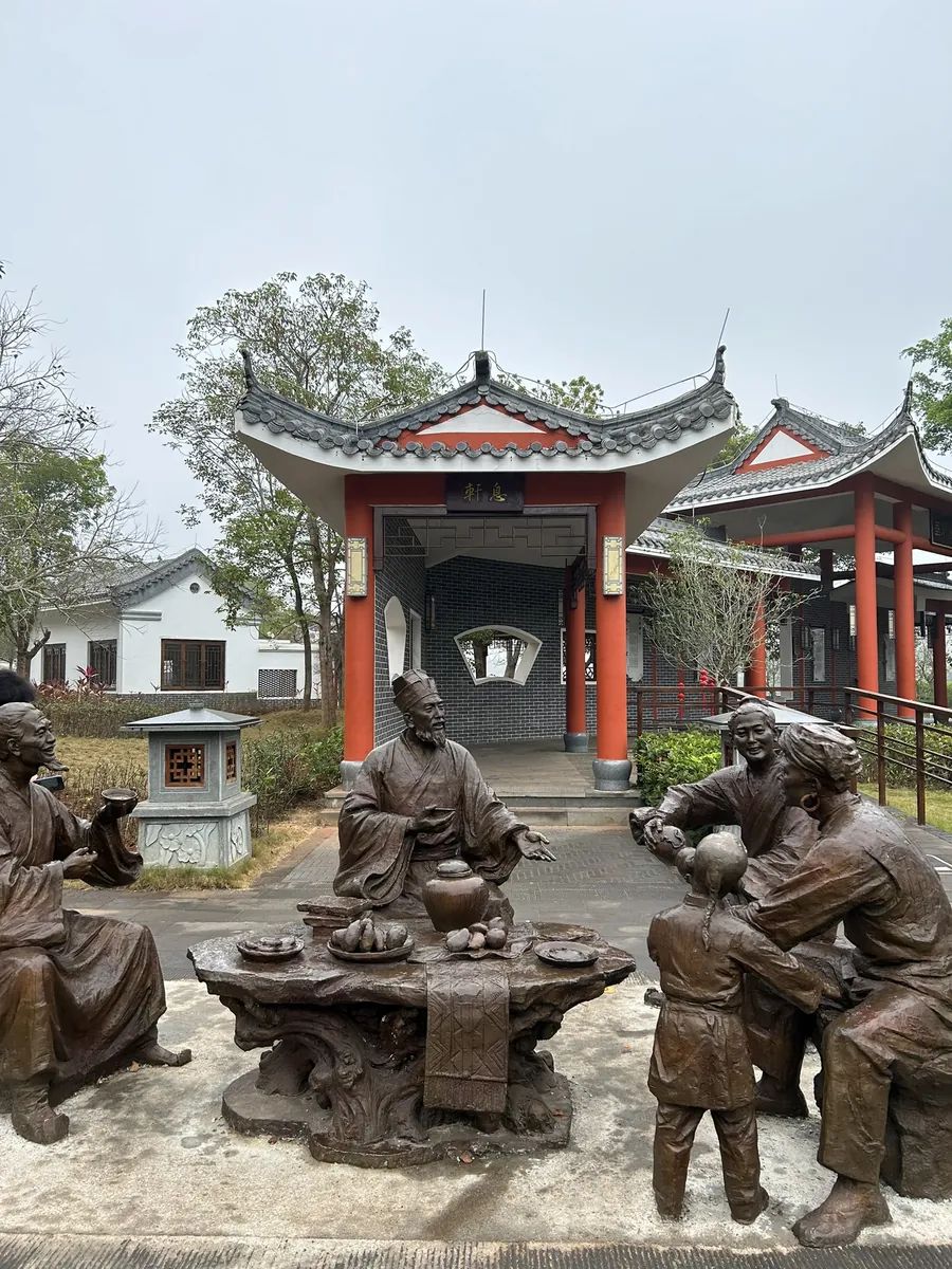 Bronze figures of the exiled poet Su Dongpo sharing wine with locals in the garden of the Dongpo Academy in Danzhou, western Hainan, before a red-columned pavilion.