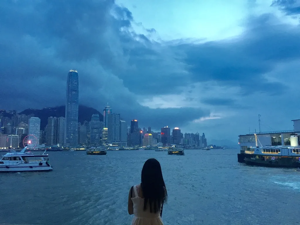 Victoria Harbour at blue hour seen from the Tsim Sha Tsui promenade, with the Hong Kong Island skyline and the Star Ferry pier.