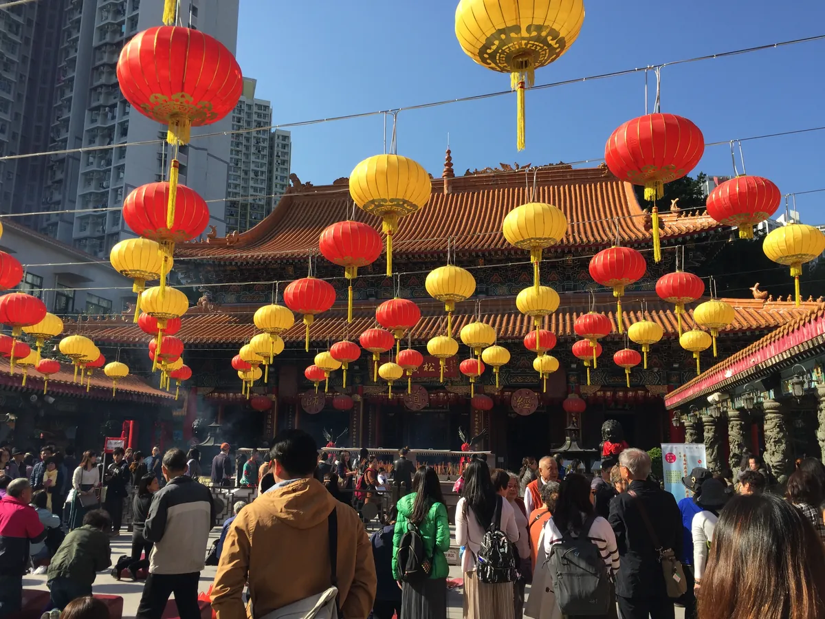 The red and gold buildings of Wong Tai Sin Temple in Hong Kong, hung with rows of festival lanterns, busy with visitors.