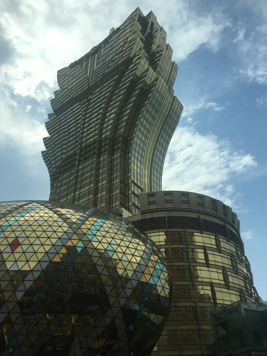 The gleaming golden lotus-shaped tower of the Grand Lisboa casino in Macau rising above a mirrored glass dome against a bright sky.