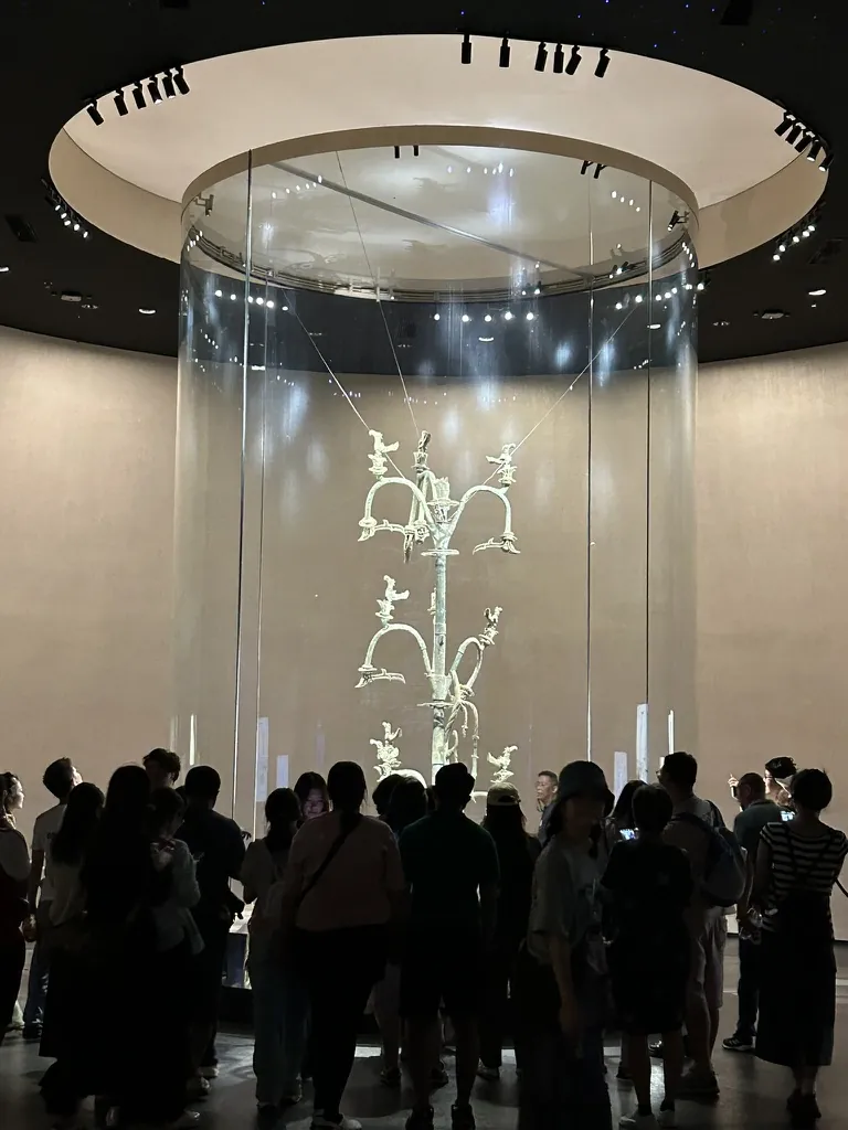 Visitors silhouetted before the illuminated bronze sacred tree in its glass case at the Sanxingdui Museum near Chengdu.