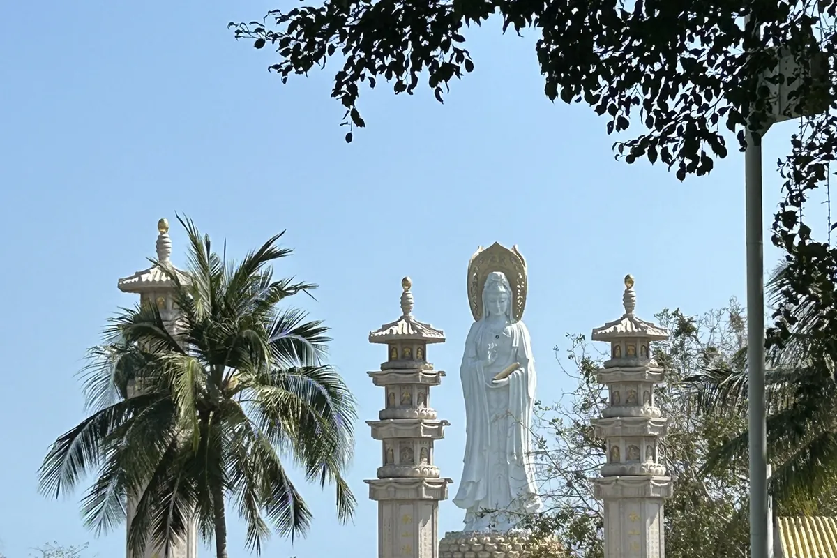 The towering white Nanshan Sea Guanyin statue in Sanya, Hainan, framed by stone pagodas and coconut palms against a bright blue tropical sky.