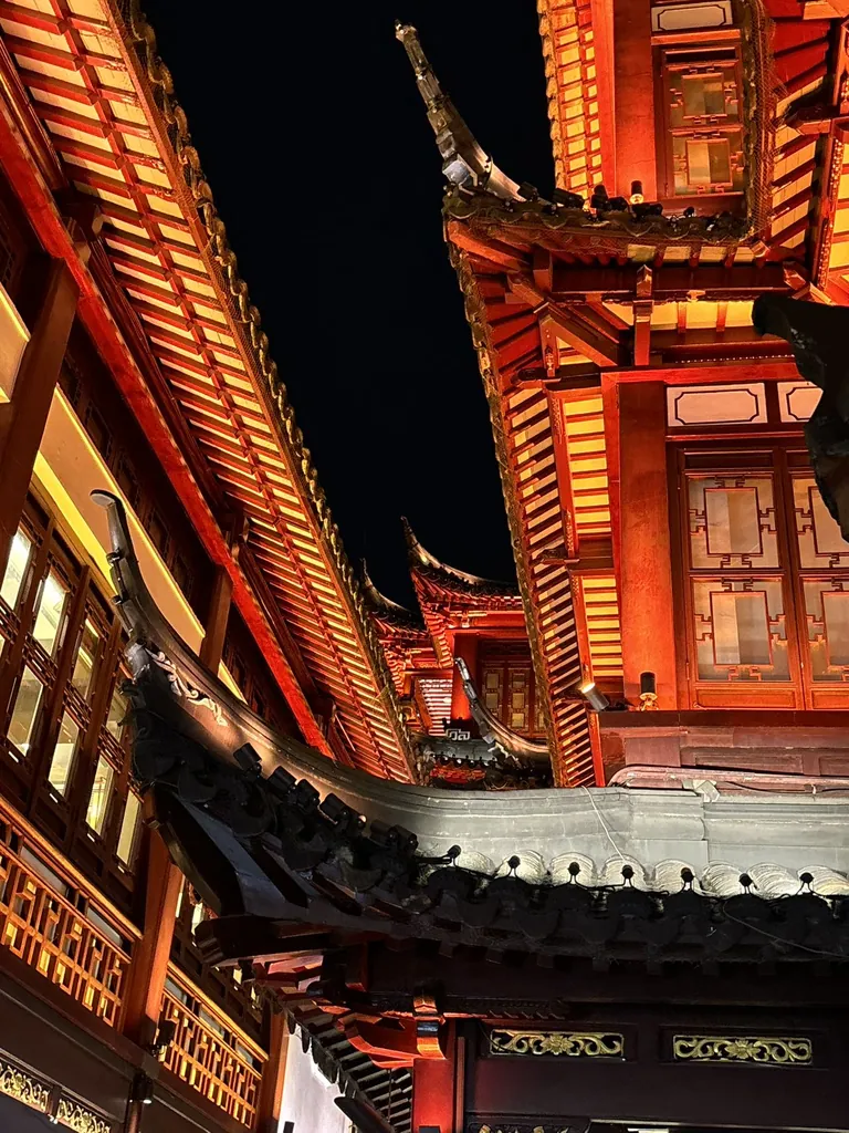 The red-and-gold upturned eaves of the City God Temple bazaar in Shanghai's Yu Garden, lit warmly against the night sky.