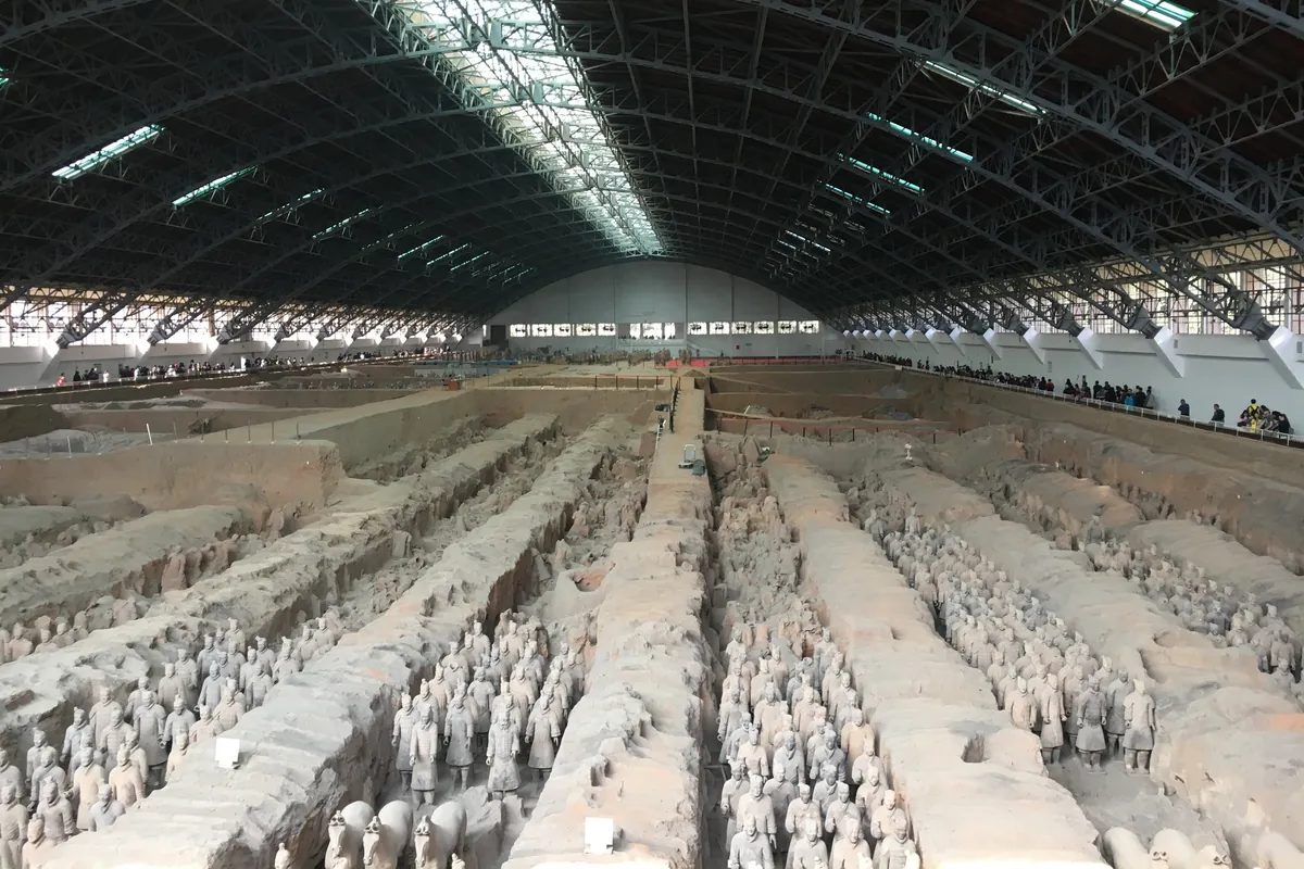 Rows of terracotta warriors in Pit 1 of the Terracotta Army excavation hall near Xi'an, beneath a vaulted skylight roof.