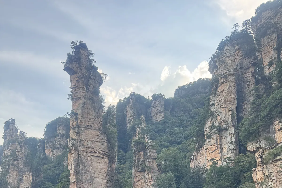 A towering quartz-sandstone pillar of Wulingyuan rising from the forest in Zhangjiajie — the "Avatar" mountains — with more columns behind it.